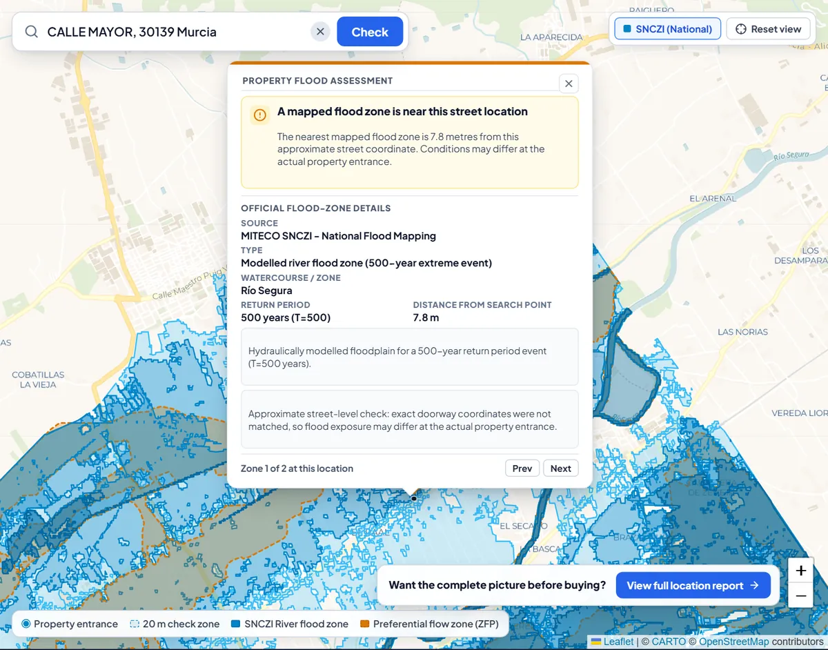 Flood check for a street in Murcia: the result card says a mapped flood zone is near the street location, 7.8 metres away, with shaded national flood zones on the map