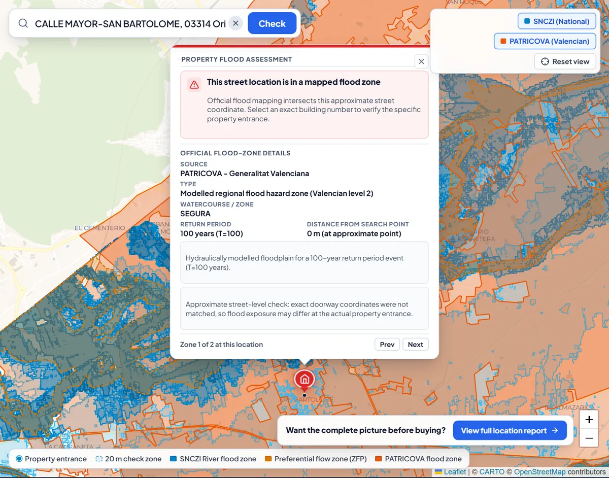 Flood check for a street in Orihuela: the marker sits inside shaded official flood zones and the result card says the street location is in a mapped flood zone